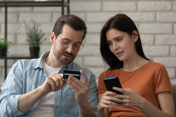 Believe me, it is easy. Confident husband teaching interested young wife to make cashless payment using mobile banking app. Millennial male explaining female how to enter plastic card details online