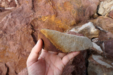Hand holding a piece of sandstone rock on nature background. 