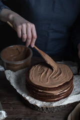 making a chocolate cake from thin cakes. The woman decorates the cake with cream.