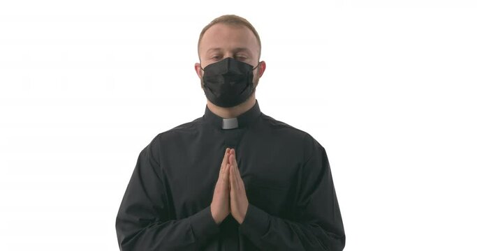 Portrait of Caucasian priest in face mask folding hands in pray and lifting eyes up in a plea. Begging for mercy during pandemic. Prayer hands. Isolated on white background