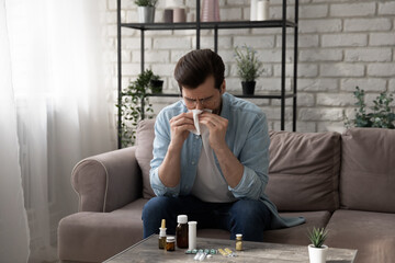 On sick leave. Ill young man stay at home on workday sneezing feeling bad catching cold flu....