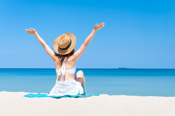 Rear view of  woman wearing sun hat and white bikini spends vacation at the beach on a white sand. summer beach concept