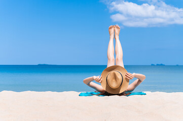 Fototapeta na wymiar Rear view of woman wearing sun hat and white bikini spends vacation at the beach on a white sand. summer beach concept