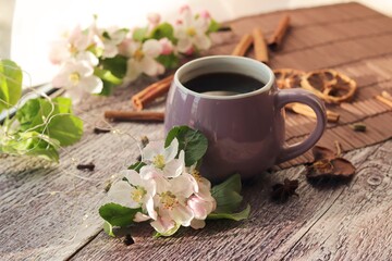 Obraz na płótnie Canvas Cup of coffee with spices, flowering branches on a wooden table against the background of a window, spring, the concept of home comfort, morning