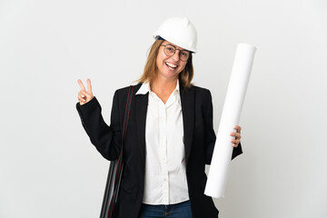 Middle age architect woman with helmet and holding blueprints over isolated background smiling and showing victory sign