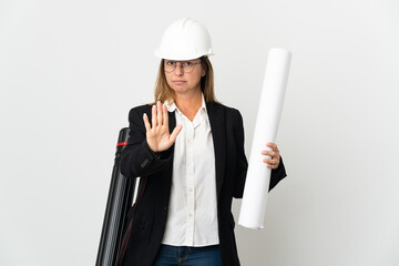 Middle age architect woman with helmet and holding blueprints over isolated background making stop...