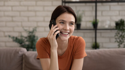 Delightful conversation. Happy positive young lady sitting on sofa at living room speaking by phone...