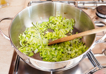 Leek cooking in a pan with extra virgin olive oil. Wooden spoon. Cooking at home