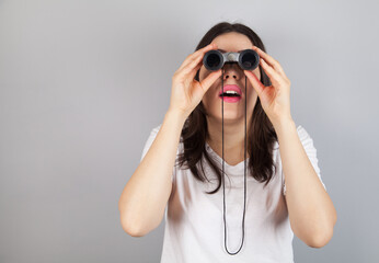 Young beautiful woman an a gray background with binoculars.