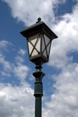 Fototapeta na wymiar Black and white lamp post with street lantern in retro style in front blue sky with white clouds on bright sunny day vertical view closeup