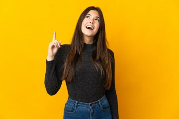 Teenager Brazilian girl isolated on yellow background pointing up and surprised