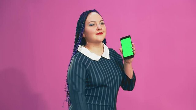 Stylish brunette with blue afro braids is dancing with a phone in her hands a green screen