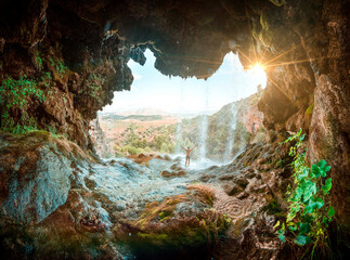 Image inside a cave with a waterfall and the silhouette of a man opening his arms. The essence of...