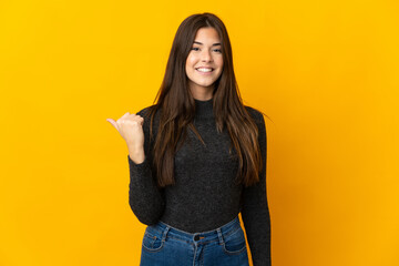 Teenager Brazilian girl isolated on yellow background pointing to the side to present a product