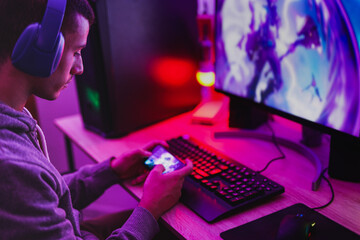Young boy wearing headset and play video games with smartphone online in front of computer - Home isolated for coronavirus outbreak