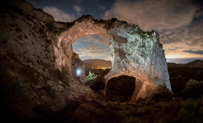 Panoramic of two arches sculpted in the mountain. The silhouette of a man illuminates two large stone arches. The Arches, Alicante. Night landscape of the stone arches, the stars illuminate the scene