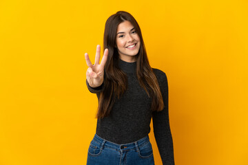 Teenager Brazilian girl isolated on yellow background happy and counting three with fingers