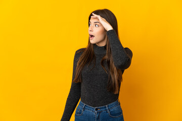 Teenager Brazilian girl isolated on yellow background with surprise expression while looking side