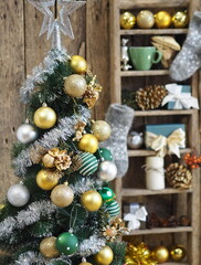 Christmas tree decor in golden yellow and green style on blurred background of retro shelves with New Year is baubles and Christmas socks.