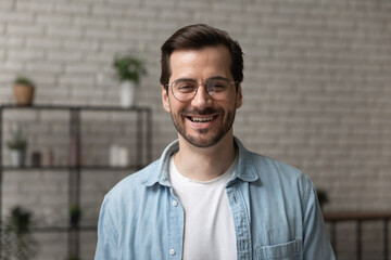 Headshot portrait of happy young man looking at camera standing indoors at home or modern office....