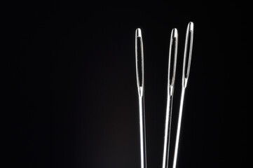 three sewing needles without thread on a dark background. macro.