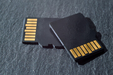 two micro sd cards lie on top of each other on a dark textured background, with golden contacts at...