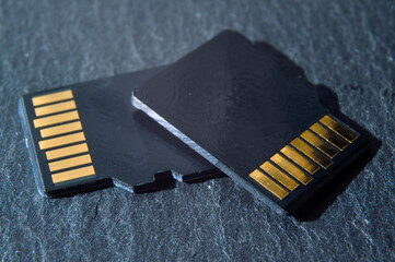 two micro sd cards lie on top of each other on a dark textured background, with golden contacts at...