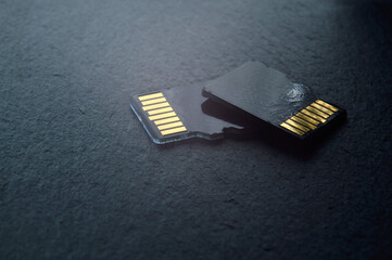 two micro sd cards lie on top of each other on a dark textured background, with golden contacts at...