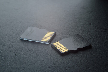 two micro sd cards lie on a dark textured background, with golden contacts at the top. close-up.