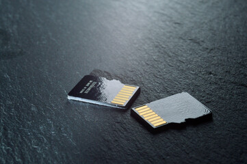 two micro sd cards lie on a dark textured background, with golden contacts at the top. close-up.