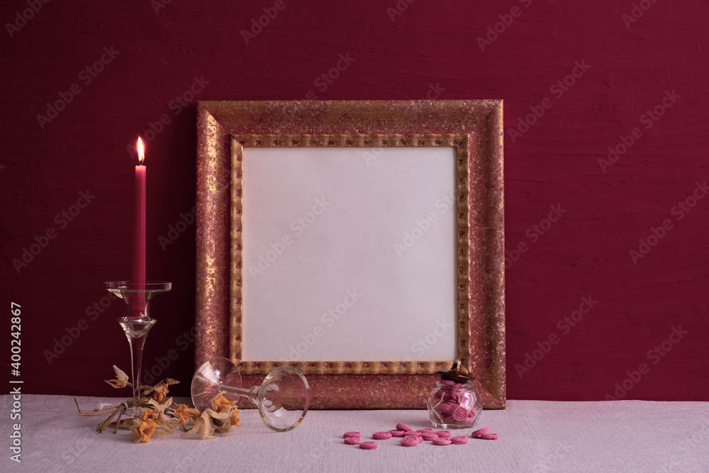 Wall mural dry daffodils, a long-stemmed candlestick and a candle burning, an old photo frame on red and a deco