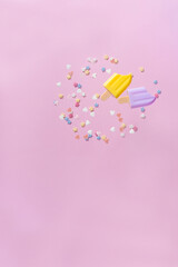 Ice cream popsicles with colorful sugar decoration on pastel pink paper background.