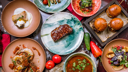 Assorted dishes on talbe. juicy Ribeye steak, burgers with meat, shrimps on grill, fish, salad top view