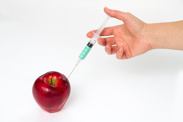 A hand with a syringe injected into a red apple