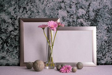 pink gerberas in a transparent vase, gray photo frames and decor on a gray background