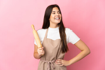 Teenager Brazilian girl holding a rolling pin isolated on pink background posing with arms at hip and smiling