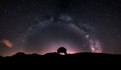 The silhouette of a man at night holding a Neolithic stone arch, observing the stars and the Milky...