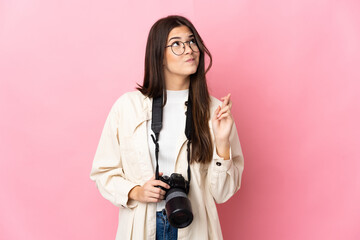 Young photographer Brazilian girl isolated on pink background with fingers crossing and wishing the...