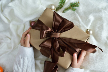 Girl's hands in white pullover holding gift box with brown ribbon on white background.Happy excited girl child holding christmas gift box. Christmas, New Year, Valentine's day and birthday concept.