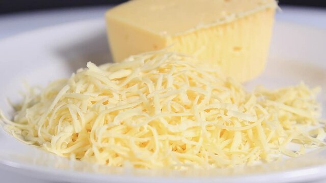A piece of hard cheese and a piece of grated cheese on a light plate. Close-up.