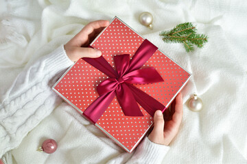 Girl's hands in white pullover holding gift box with red ribbon on white background.Happy excited girl child holding christmas gift box. Christmas, New Year, Valentine's day and birthday concept.