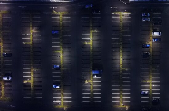 Gro&szlig;er mit Laternen beleuchteter Parkplatz mit wenigen Autos aus der Vogelperspektive
