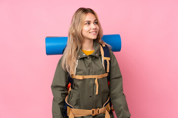 Teenager Russian mountaineer girl with a big backpack isolated on pink background laughing