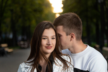 Fototapeta premium Portrait of beautiful young couple in park. Guy gently touches the girls hair with his nose. Tenderness