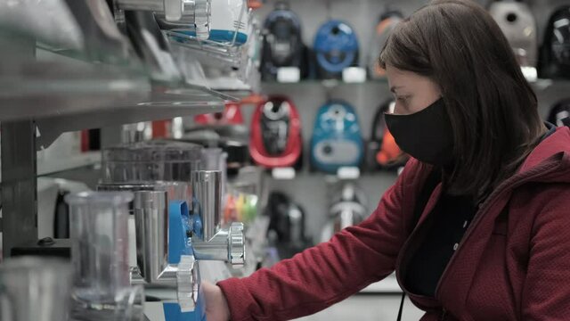 Girl in a protective mask against the virus, chooses an electric meat grinder in the store. The concept of shopping during a pandemic and epidemic