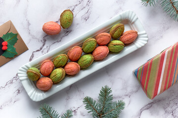 Walnut shaped Cookies with Dulce De Leche. Tasty creative dessert in green and red on marble table with winter decorations, fir twigs and ribbons with snowflakes. Gift box wrapped in craft paper.