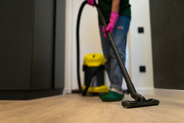 Fototapeta premium Woman vacuuming the parquet floor in the room with professional vacuum cleaner. Cleaning company employee cleans the house