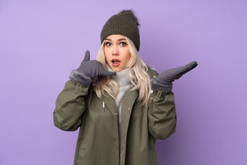 Teenager blonde girl with winter hat over isolated purple background making phone gesture and doubting