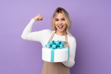 Young pastry chef holding a big cake over isolated purple background making strong gesture