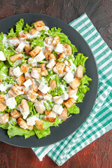 top view caesar salad on oval plate green white checkered tablecloth on dark red background